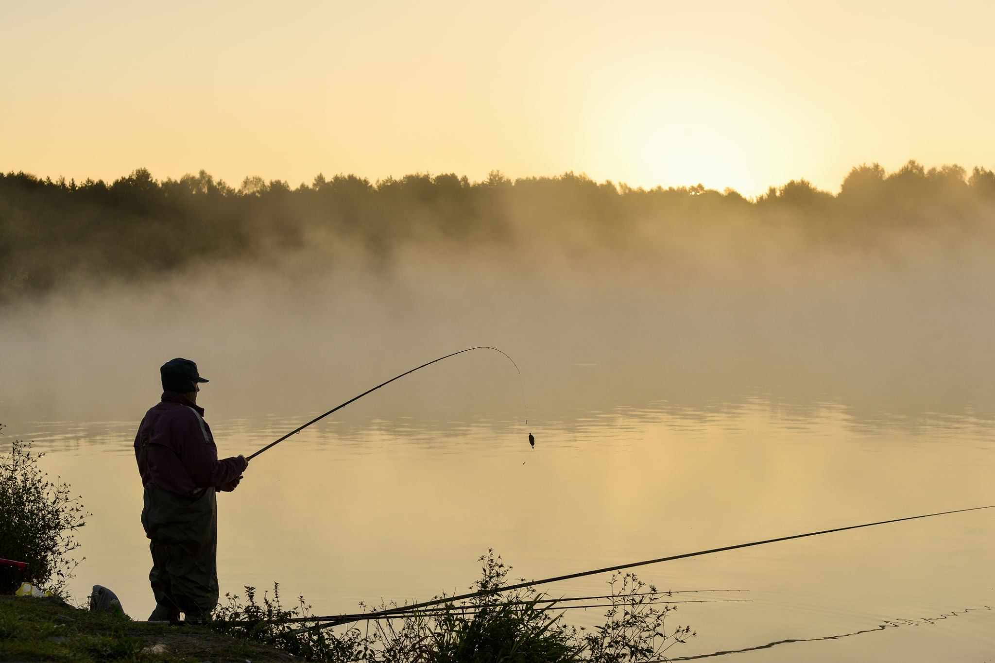Angler silhouette against misty morning lake.