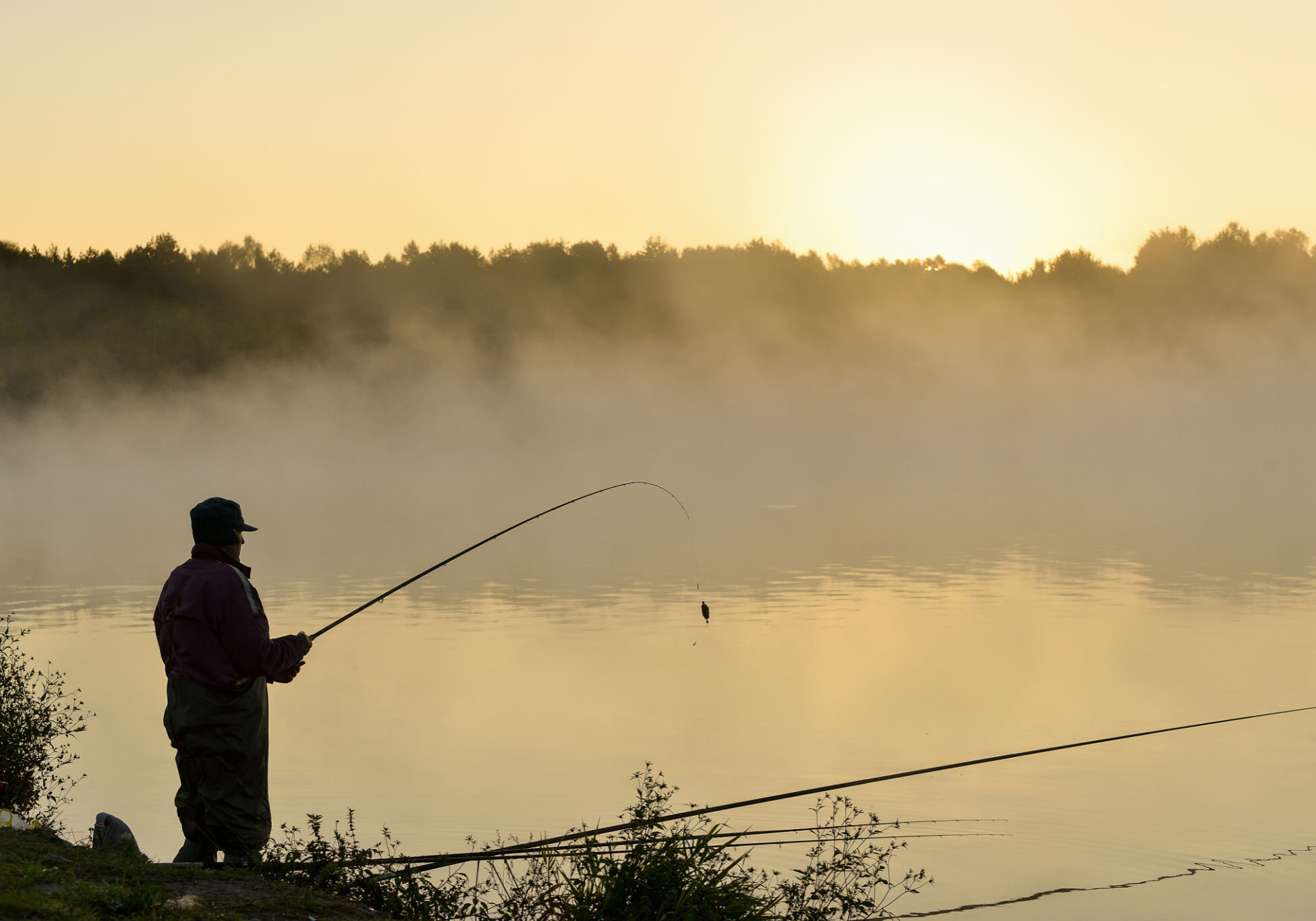 Angler silhouette against misty morning lake.